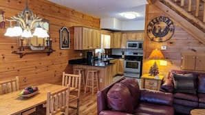 A cozy cabin interior with a wooden dining area, a leather sofa, a kitchen with wooden cabinets, and a staircase. - "Rushing Bear!"   Fully furnished two bedroom cozy cabin you want to capture!" (Maggie Valley)
