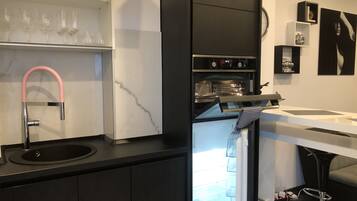 A modern kitchen with a black countertop, a marble backsplash, a built-in oven, and a stainless steel sink.