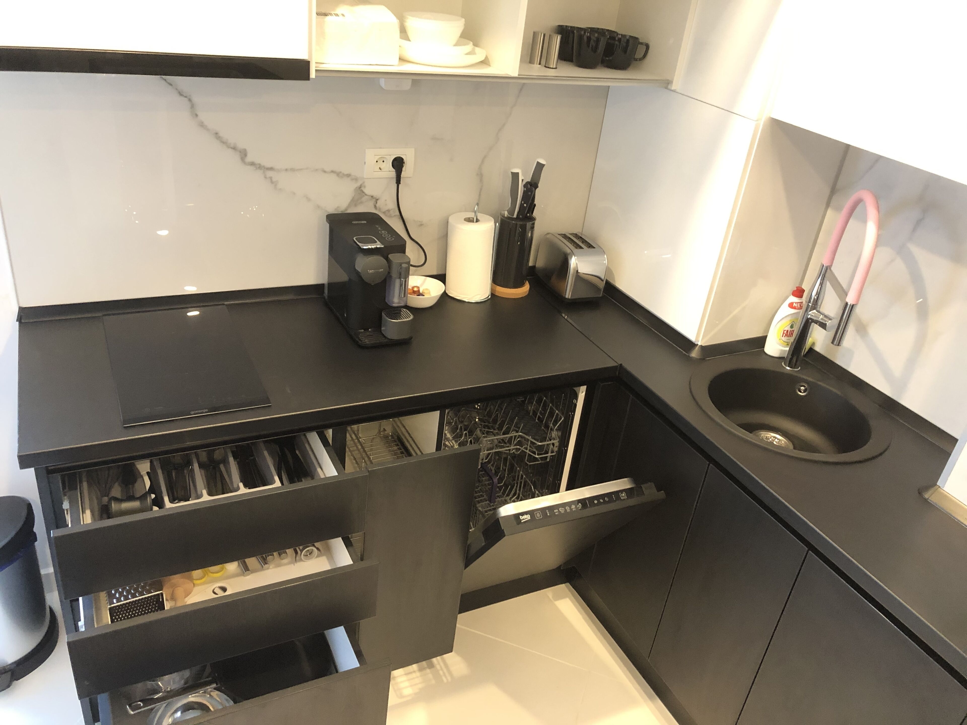 Una cocina moderna con encimera negra, lavavajillas integrado, fregadero y cafetera.