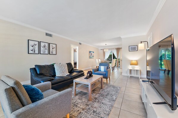 A modern living room with a black leather sofa, grey armchairs, a wooden coffee table, and a flat-screen TV. - Spacious Beach Apt Walking Distance to Everything (Singer Island)