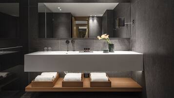 A modern bathroom with a large mirror, a white sink, and three wooden trays with towels.