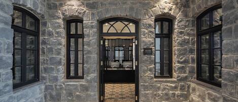 Un pasillo de paredes de piedra con ventanas arqueadas y un acceso central a un baño.