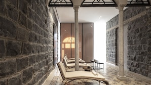 Habitación de paredes de piedra con sillones y una pequeña mesa, que cuenta con un ventanal y una puerta al fondo.