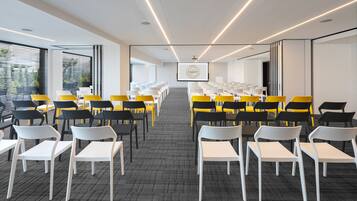 A conference room with rows of chairs, a projector screen, and a large window with blinds.