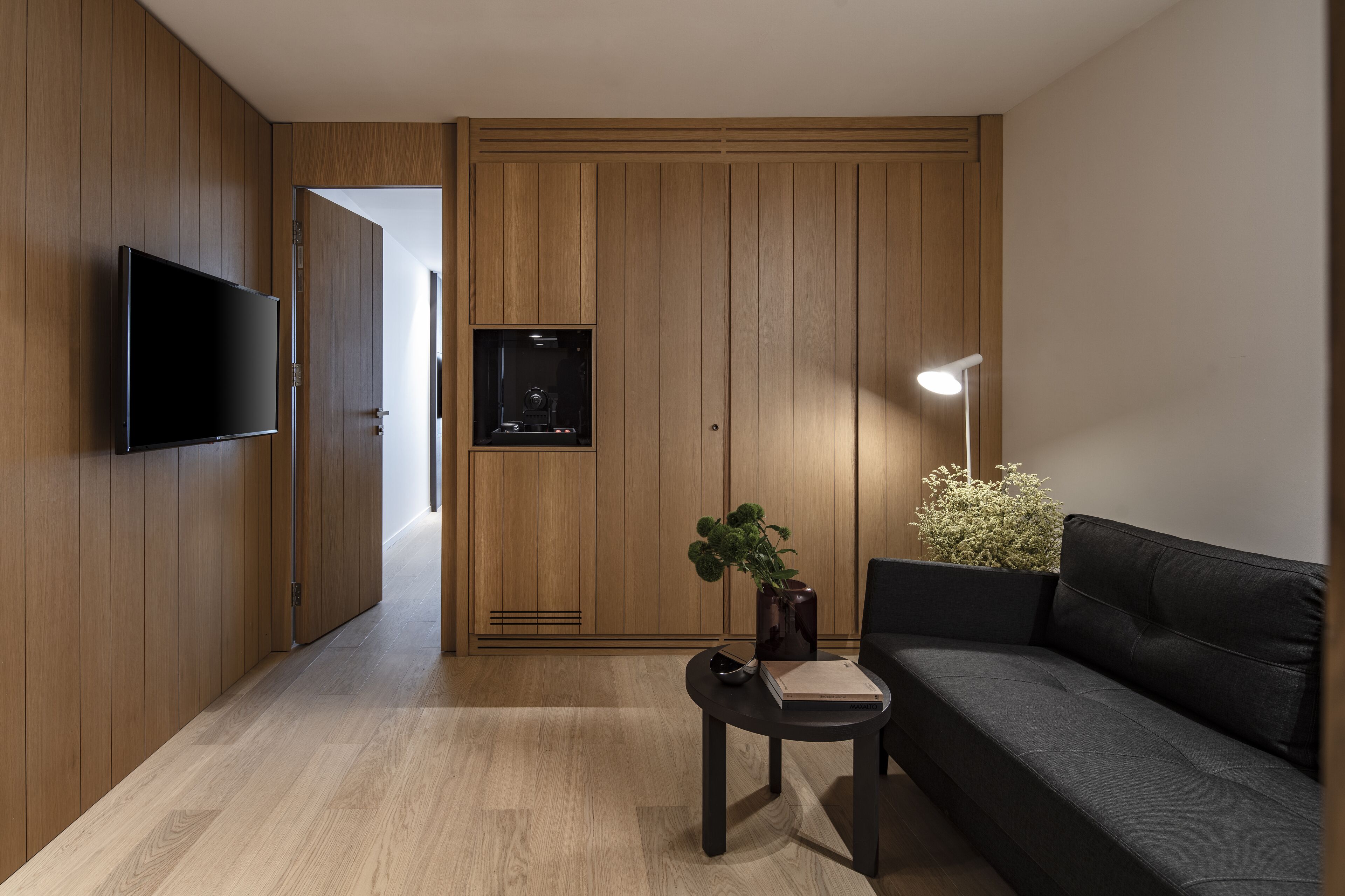 Un soggiorno moderno con una TV a schermo piatto, un divano scuro, un tavolino con un vaso e un libro, e pannelli in legno.