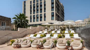Un hôtel moderne doté d’un espace piscine comprenant des chaises longues et des parasols.