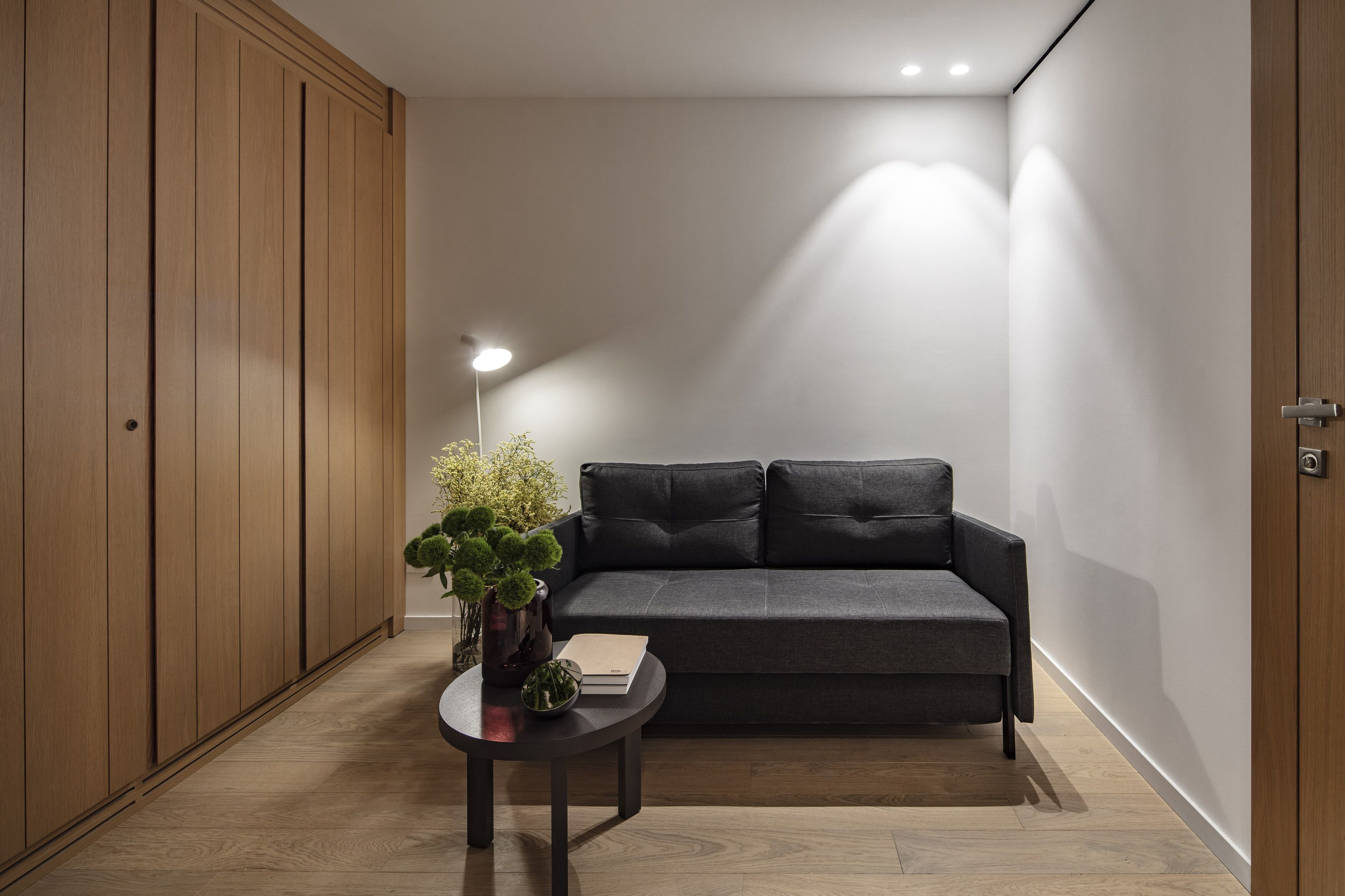 Una sala de estar moderna con un sofá gris oscuro, una mesita redonda con un florero de plantas verdes, y un libro.