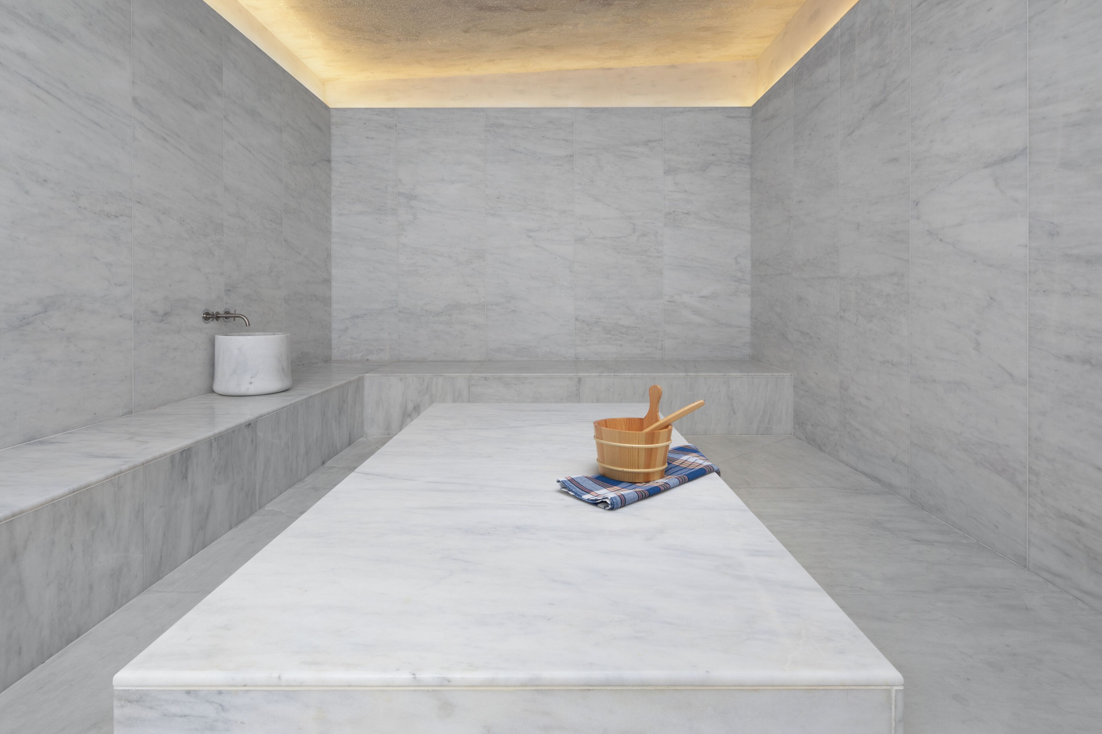 Un baño moderno con un lavamanos de mármol, un cubo de madera y una toalla.