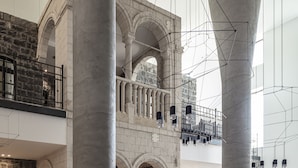 Un vestíbulo espacioso con techos altos, grandes columnas de piedra y una escalera moderna.