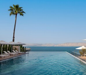 A pool with lounge chairs and umbrellas, a palm tree, and a view of the sea and mountains. - Sofia Hotel Sea of Galilee (Tiberias)