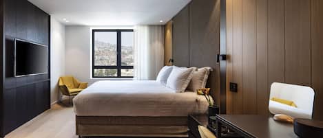 Une chambre d’hôtel moderne dotée d’un grand lit, d’une télévision à écran plat, d’un bureau avec une chaise et offrant une vue sur la ville par la fenêtre.