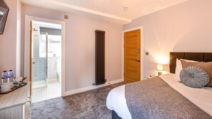A bedroom with a bed, bedside table, lamp, and a view of the bathroom. - Bondgate Hotel East Midlands Airport (Derby)