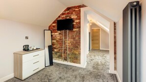 A bedroom with a brick wall, a flat-screen TV mounted above a dresser, and a radiator on the right. - Bondgate Hotel East Midlands Airport (Derby)
