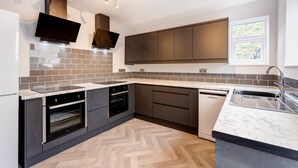 A modern kitchen with dark cabinets, a built-in oven, a dishwasher, and a large window providing natural light. - Bondgate Hotel East Midlands Airport (Derby)