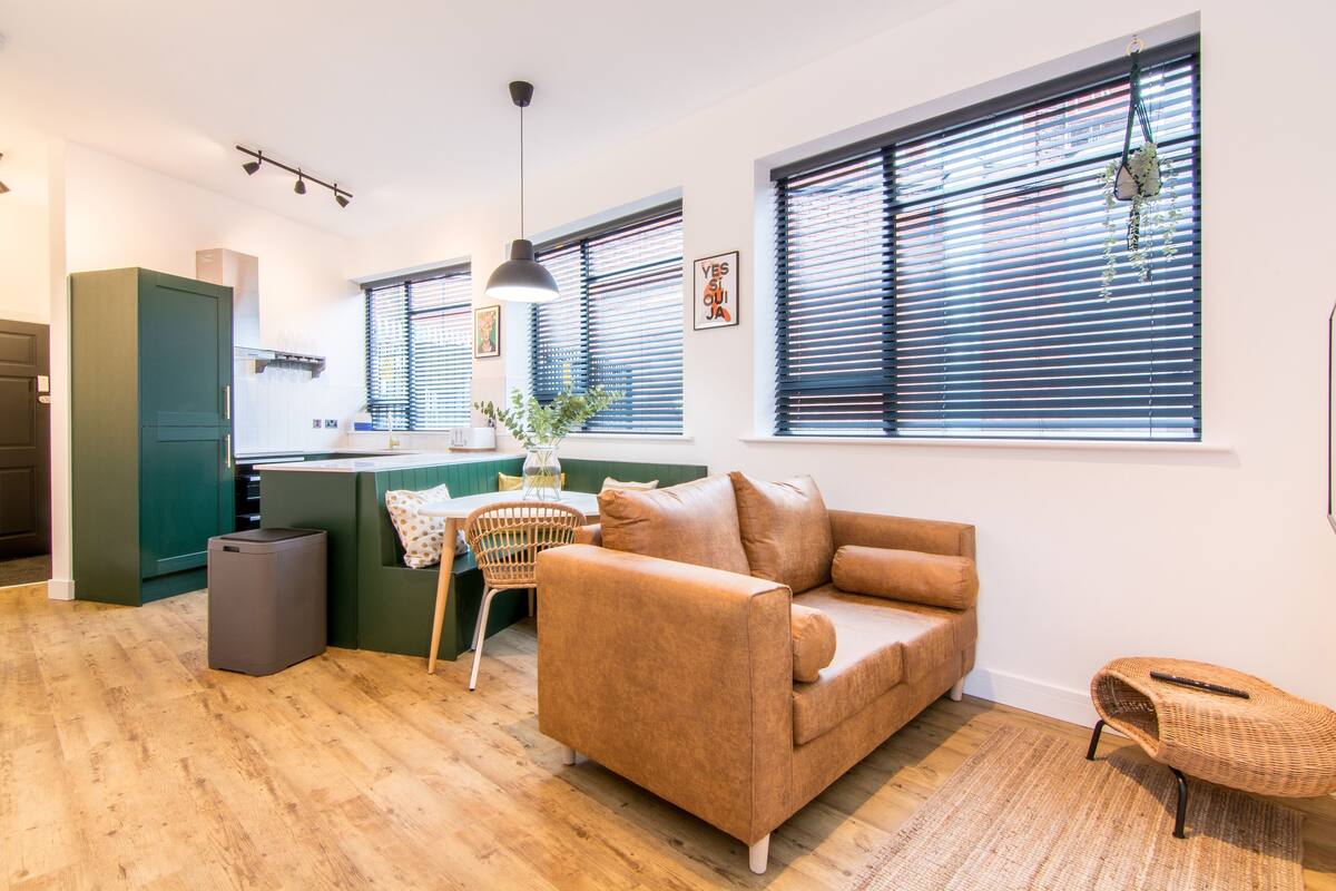 A modern kitchen with a dining area, a sofa, and a wicker chair.