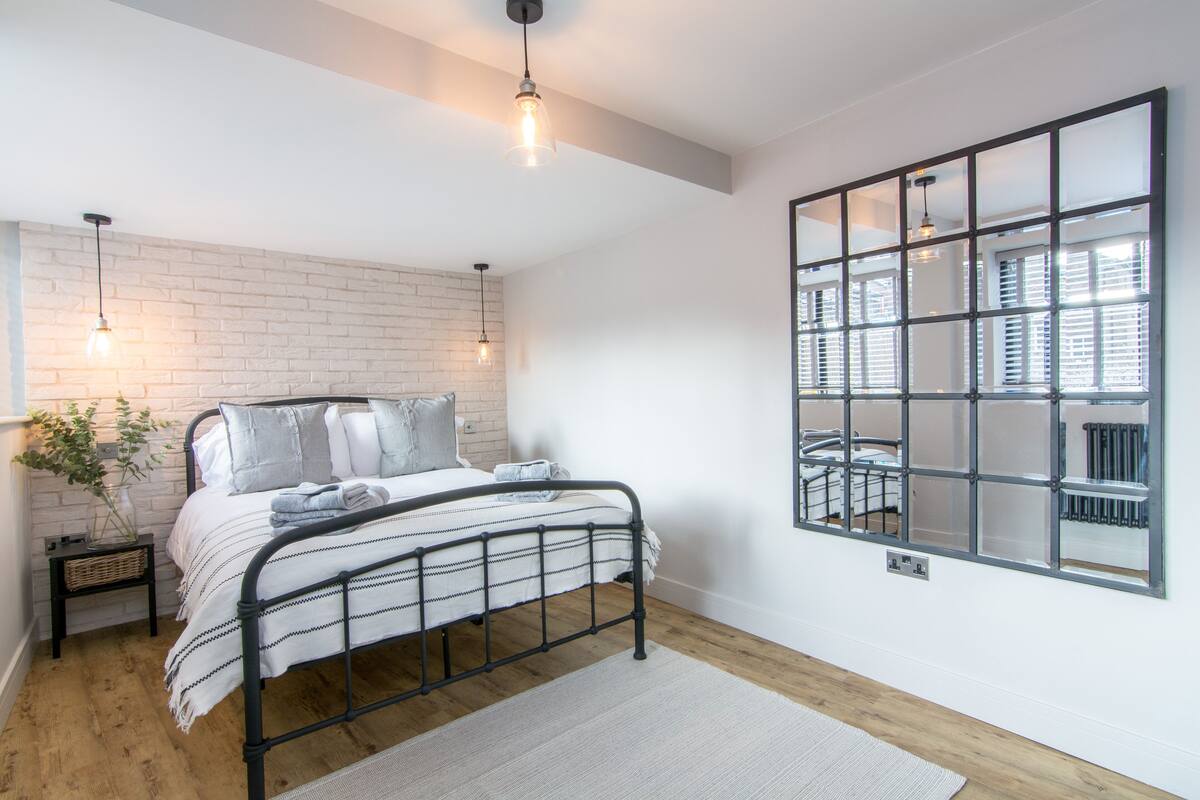A modern bedroom with a metal bed frame, a white brick accent wall, and a large window with blinds.