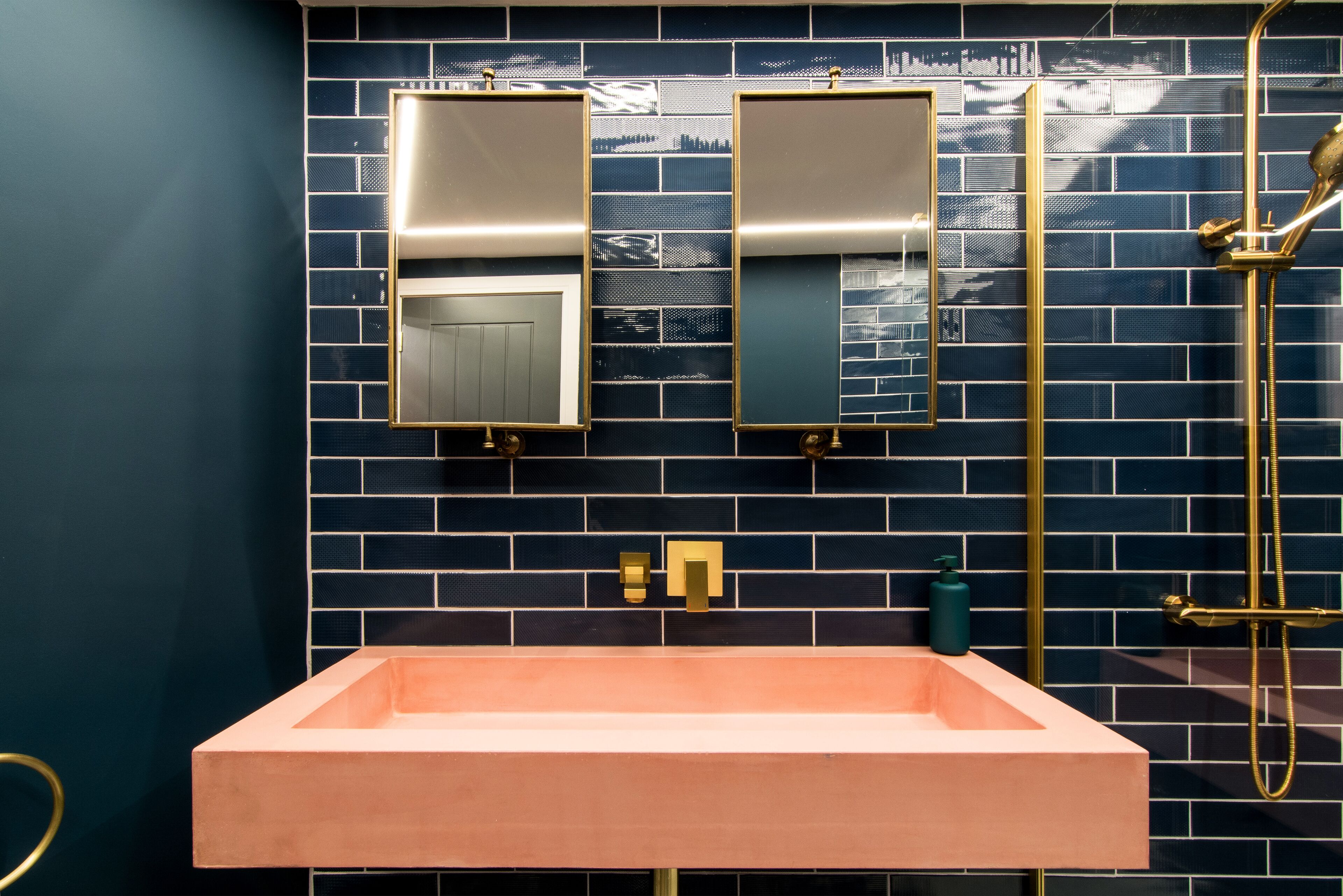 Ein Badezimmer mit blauen Fliesen, einem rechteckigen Waschbecken mit goldfarbenem Wasserhahn und einer goldfarbenen Duscharmatur.
