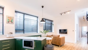 Una cocina moderna con armarios verdes, horno empotrado y un ventanal con persianas.