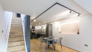 Una cocina moderna con salpicadero de ladrillo, un comedor con mesa y sillas redondas, y una escalera que sube a otro nivel.