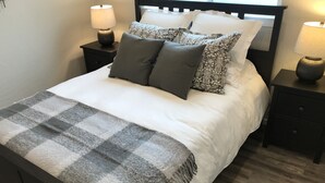 A neatly made bed with a checkered blanket, two bedside tables with lamps, and a headboard.