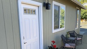 A building with a white door, a window, and a porch with chairs and potted plants.