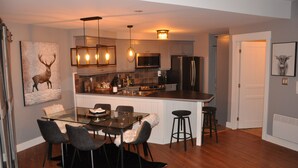 A modern kitchen with a central island, bar stools, and a dining table with chairs. - Cozy Condo in the Heart of Mont Tremblant Resort                (Mont-Tremblant)