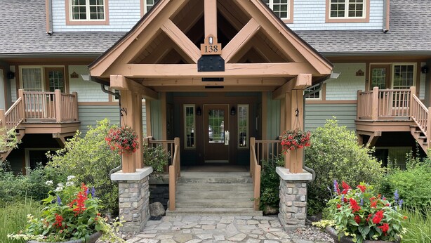 A two-story house with a stone entryway, wooden porch, and a number sign above the door. - Cozy Condo in the Heart of Mont Tremblant Resort                (Mont-Tremblant)