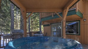 Un jacuzzi en una cabaña de madera con terraza, una parrilla y un comedor.