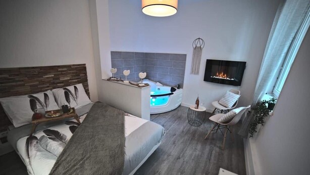 A modern hotel room with two beds, a sitting area with a small table and chairs, a fireplace, and a TV mounted on the wall. - -- Love Life -- (Mulhouse)