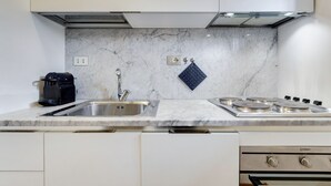 Een moderne keuken met een marmeren achterwand, roestvrijstalen apparatuur en witte kasten.