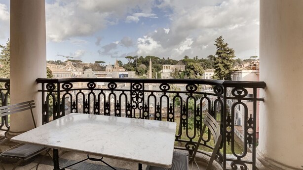 Een balkon met een marmeren tafel en bankje, met uitzicht op een stadsbeeld met historische gebouwen en bomen.