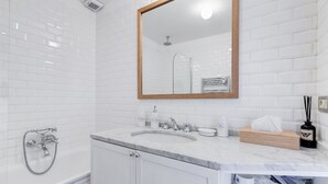 Een moderne badkamer met witte metrotegels, een marmeren wastafel, een spiegel met houten lijst en een douche met een handdouche.