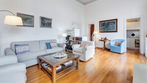 Een moderne woonkamer met een bank, fauteuils, een bijzettafeltje en een boekenkast.