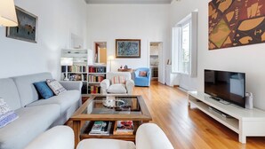 Een moderne woonkamer met een bank, salontafel en tv-meubel. Er is een boekenkast en een schilderij aan de muur.