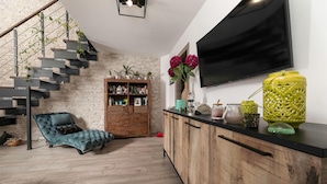 Un salon moderne avec un escalier, un canapé bleu, des meubles en bois et un téléviseur fixé au mur.