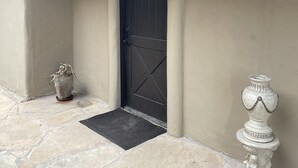 A stone-paved entrance with a dark wooden door, a potted plant, and a decorative urn.
