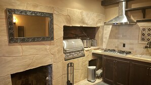 A kitchen with a stone fireplace, a built-in grill, and a large mirror.