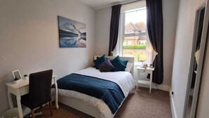 Ein Schlafzimmer mit einem Bett, einem Schreibtisch, einem Stuhl, einem Nachttisch und einem Fenster mit Vorhängen.