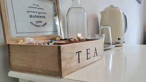 Eine hölzerne Teebox mit der Aufschrift 'TEA' auf einem weißen Tisch, zusammen mit einem gerahmten Schild, einer Karaffe und einem cremefarbenen Wasserkocher.