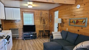 Ein gemütliches Blockhaushaus-Interieur mit Küchenzeile, einer Couch, einem Fernseher und einer Holzwand mit einem dekorativen Fischgemälde.