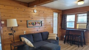 Ein gemütliches Blockhaus-Interieur mit einer Eckcouch, einem kleinen Tisch und einem Fenster mit Jalousien.
