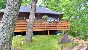 Une cabane dotée d’une terrasse en bois, entourée d’arbres et bordée d’une pelouse.
