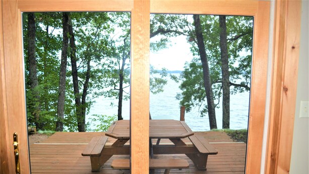 Une terrasse en bois avec des tables de pique-nique, donnant sur un lac entouré d’arbres.