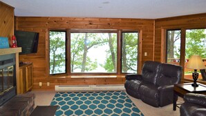 L’intérieur d’une cabane avec une cheminée, de grandes fenêtres, un canapé en cuir et un tapis à motifs.