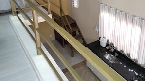 Ein Zimmer mit Treppe, Deckenventilator, Küchenzeile mit Spüle und einem fenster mit Vorhängen.