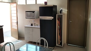 Eine kompakte Küche mit Mikrowelle, Kühlschrank und einer kleinen Arbeitsfläche. Eine Tür mit Hinweisschild '5', ein Fenster und ein Stuhl sind ebenfalls vorhanden.