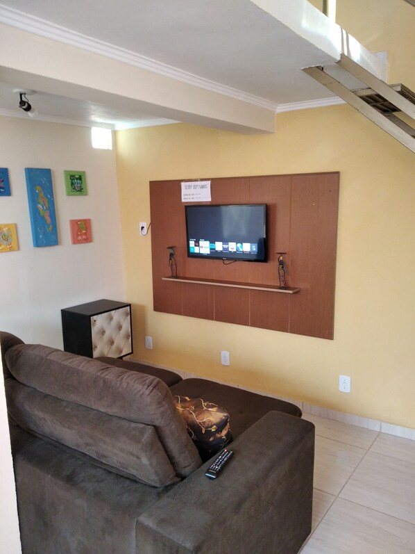 Un salon avec un téléviseur fixé au mur, un canapé et un petit meuble.