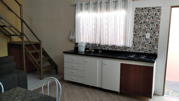 Eine kompakte Küche mit Gaskochfeld, weißen Schränken, einer Holztür und einer gemusterten Spritzschutzwand.