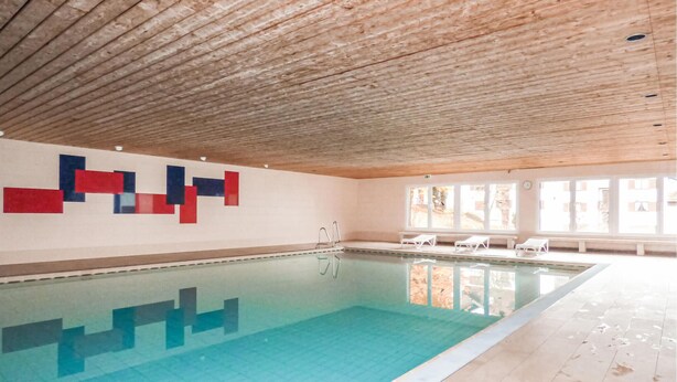 Una piscina interior con techo de madera, suelo de baldosas y pared con diseños geométricos.