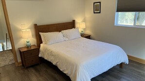 Een slaapkamer met een houten bed, twee nachtkastjes met lampen, een raam met zonwering en een lijst met een afbeelding aan de muur.